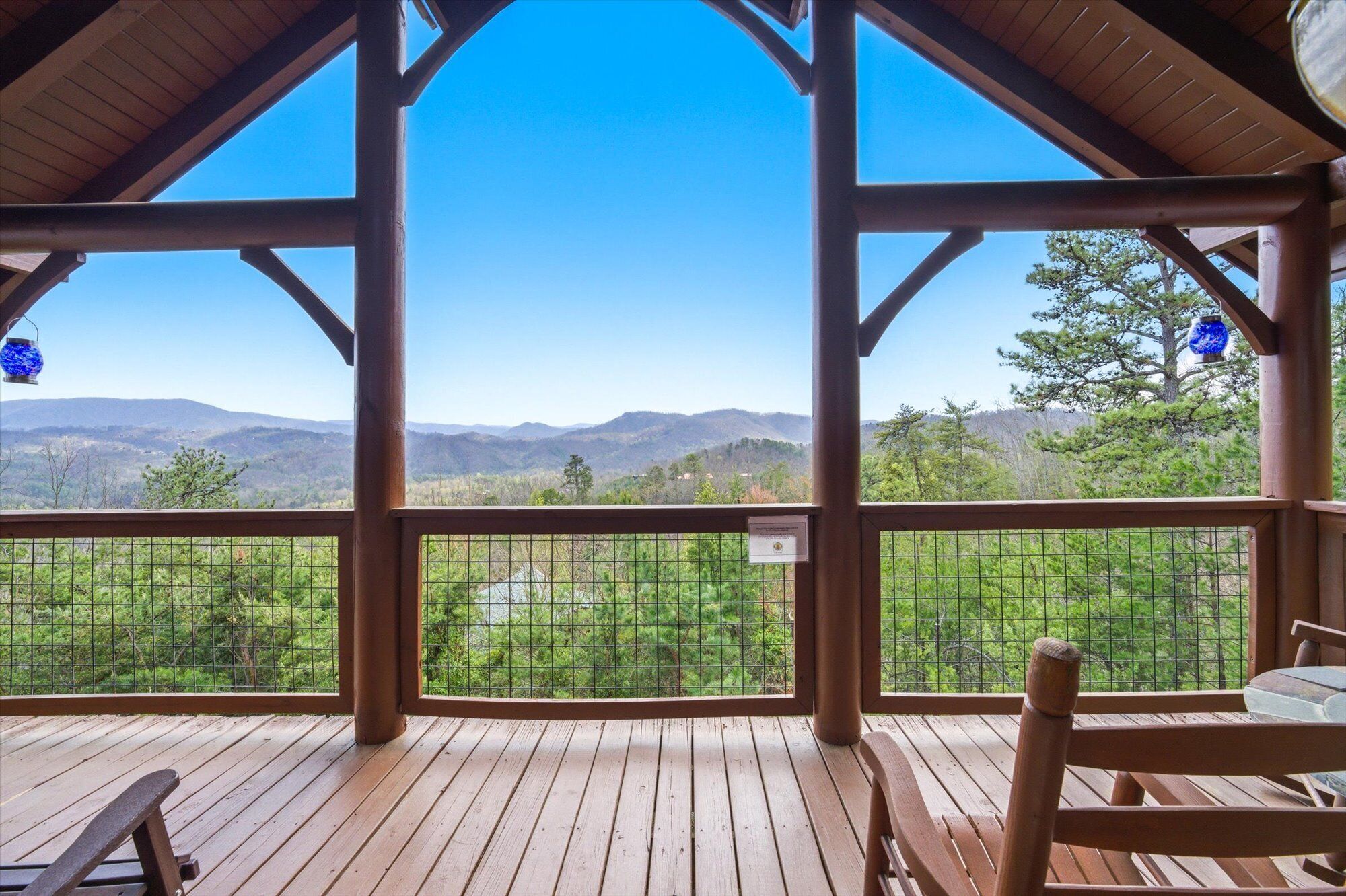 A covered wooden deck with a view of mountains and greenery.
