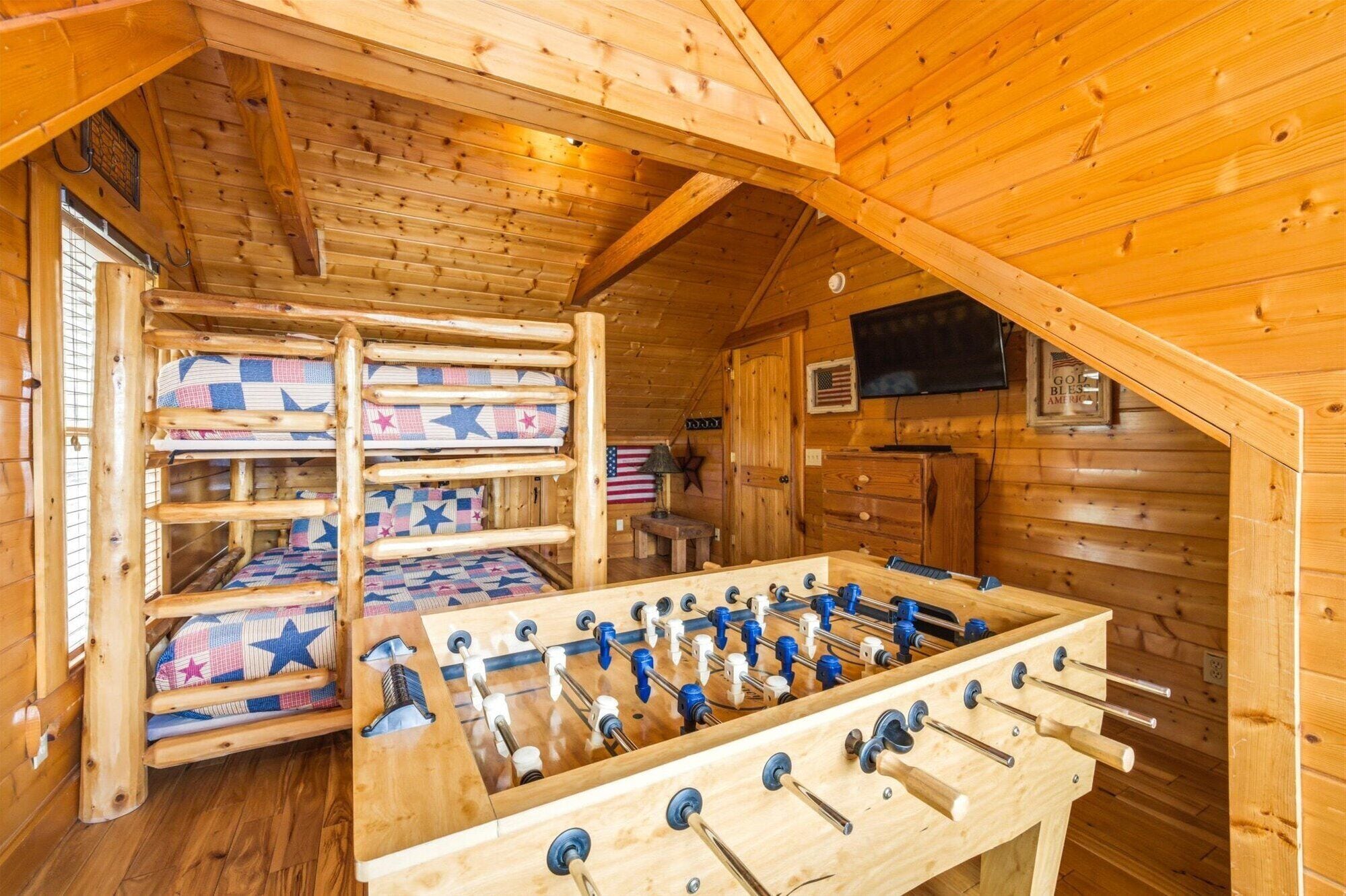 A cozy wooden cabin with bunk beds, a foosball table, and a television mounted on the wall.