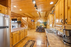 A wooden cabin interior with a kitchen, dining area, and a staircase leading to a loft. - Red, White and The View (Sevierville)