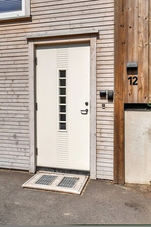 A white door with a small window, a mail slot, and a number '12' on the wall beside it. - Paradis på Sørlandet 3 (Agder)