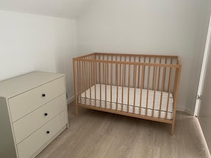 A room with a wooden crib, a white dresser with drawers, and a light-colored floor.