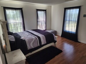 Ein Schlafzimmer mit einem Bett, einem Nachttisch, einem Fenster mit Vorhängen und Holzboden.