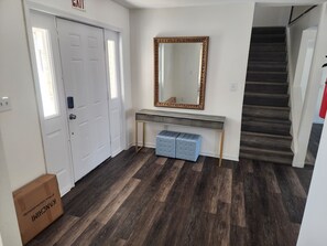 A hallway with a white door, a console table with drawers, a large mirror, and a staircase.