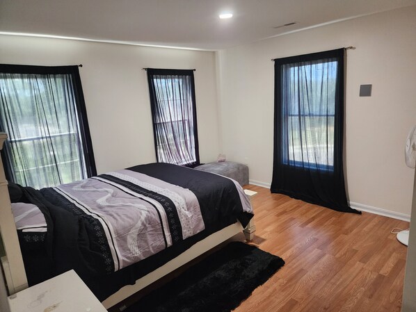 A bedroom with a bed, two windows with curtains, a bedside table, and a floor lamp.