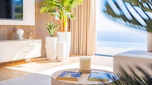 A modern living room with a large window, a potted plant, a glass candle holder, and two books on a round table. - Villa Platinum by Homie (Estreito Calheta)