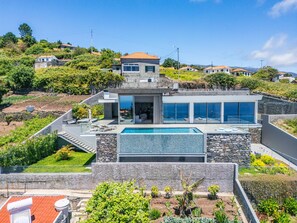 Ein modernes Haus mit Schwimmbad, Steinmauern und Blick auf die umliegende Landschaft.