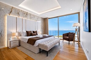 Ein modernes Schlafzimmer mit einem großen Bett, einem Nachttisch, einem Sessel und Meerblick.