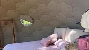 Un plafond accueillant, orné d’un motif hexagonal, dans une petite pièce comprenant un lit, des oreillers, une petite table avec une tasse rose et un cintre en bois.