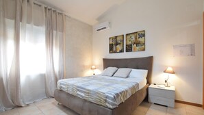 Quarto com cama, duas luminárias de cabeceira, mesa de cabeceira, ar-condicionado e obra de arte na parede.