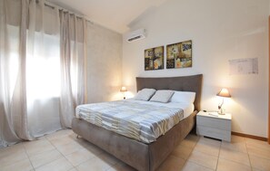 Una camera da letto con un letto, due abat-jour, un comodino, un condizionatore e opere d'arte alle pareti.