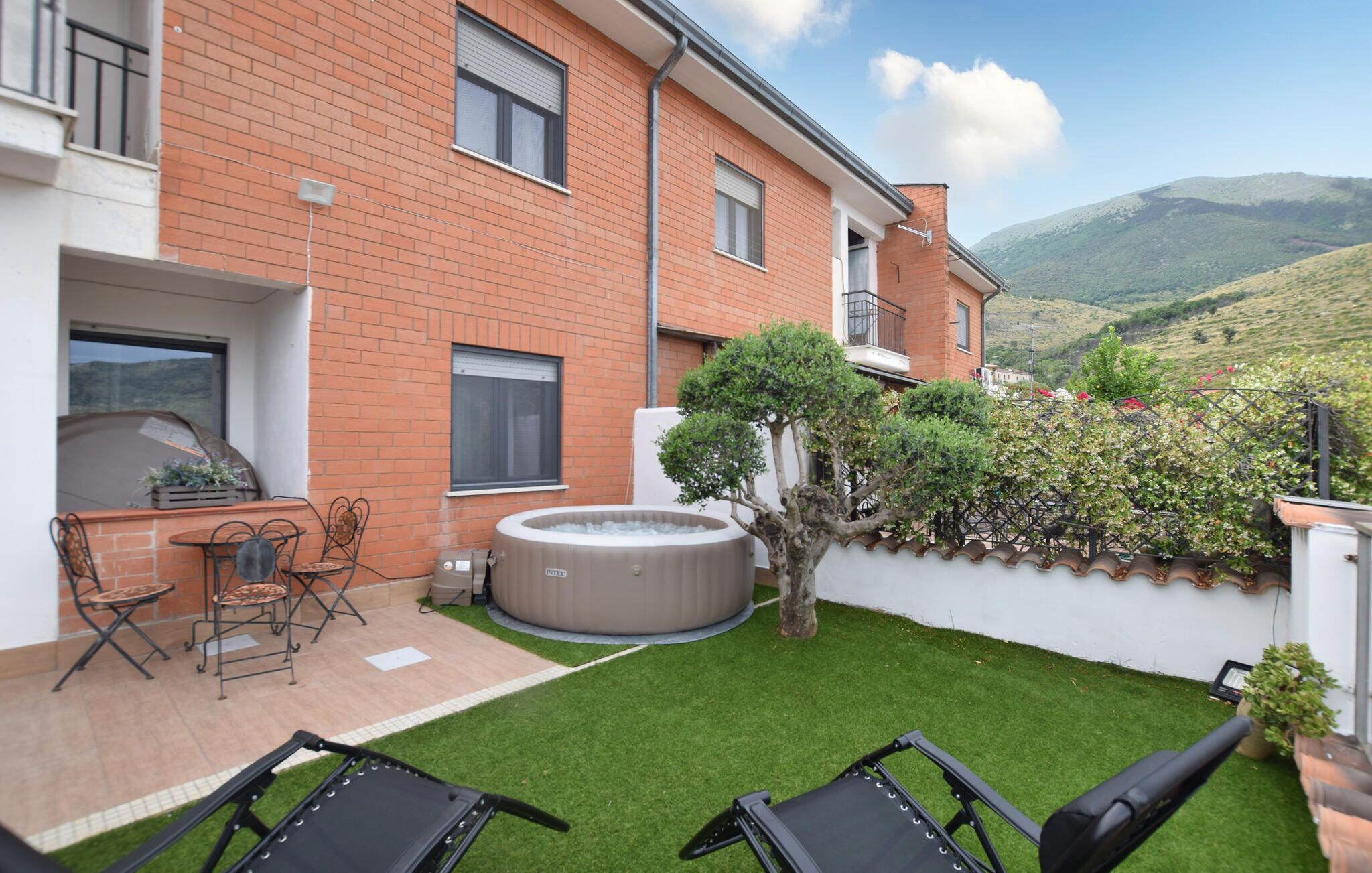Eine Terrasse mit Whirlpool, Sitzgelegenheit und Blick auf eine Hügelkuppe.