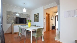 Uma área de refeições com uma mesa, cadeiras, uma TV e um vaso com flores.