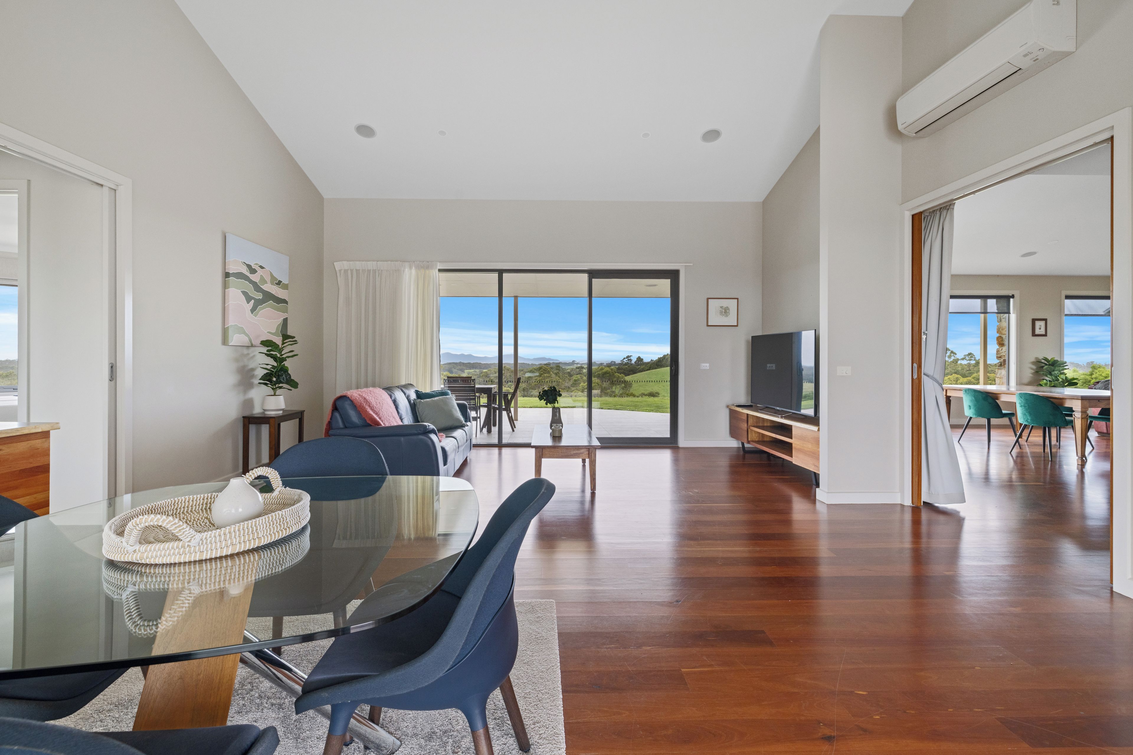 A spacious living area with a glass dining table, blue chairs, a sofa, and a television.