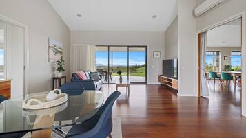 A spacious living area with a glass dining table, blue chairs, a sofa, and a television.