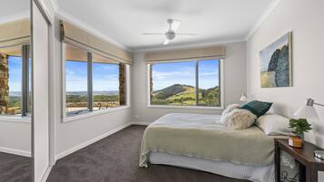 A bedroom with a large bed, a ceiling fan, and a view of a hilly landscape through the windows.