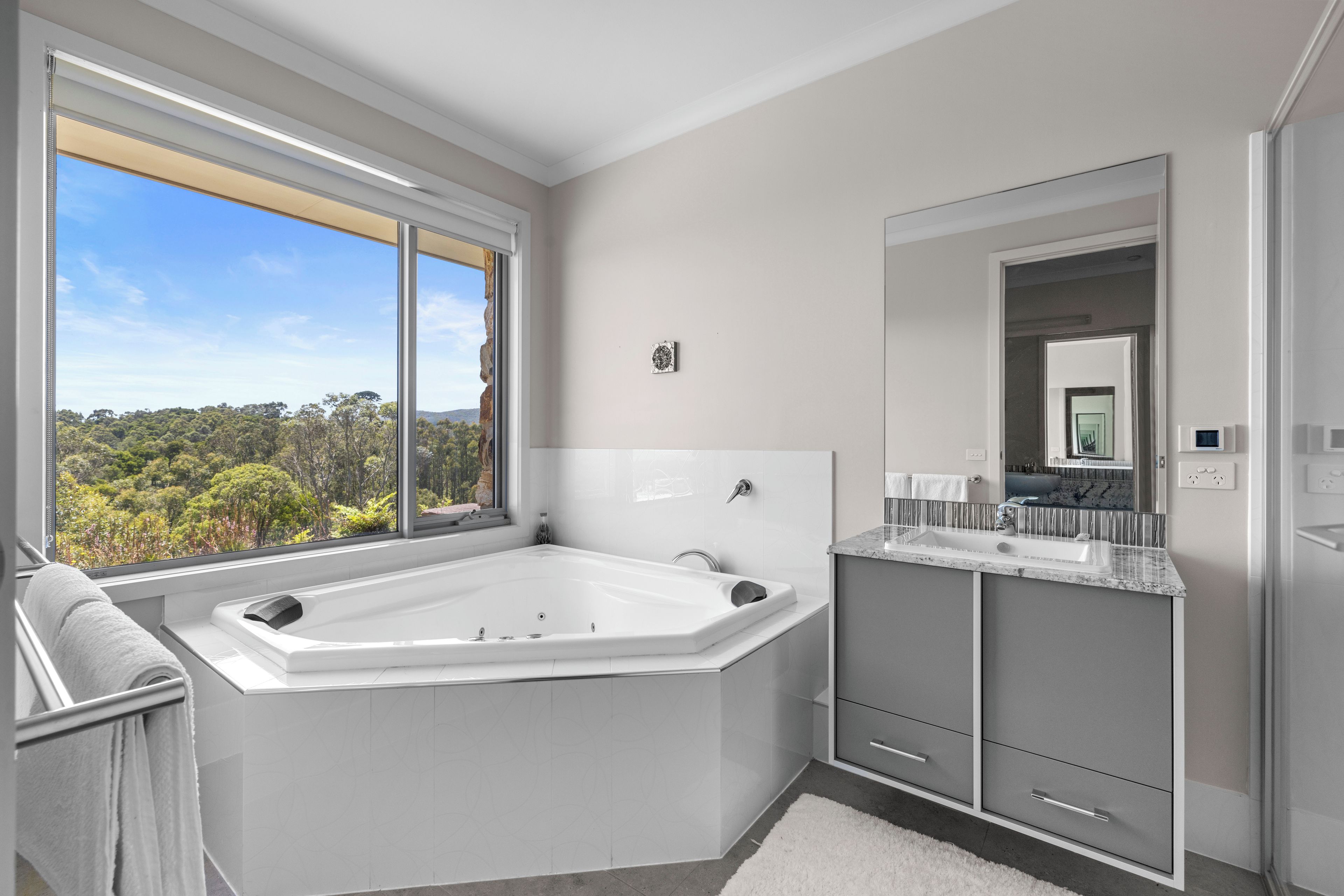 A modern bathroom with a large bathtub, a vanity with a mirror, and a view of the outdoors.