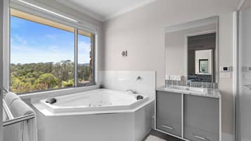 A modern bathroom with a large bathtub, a vanity with a mirror, and a view of the outdoors.