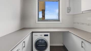 A compact laundry room with a Bosch washing machine, a small window with a view of the sea, and a tiled backsplash.