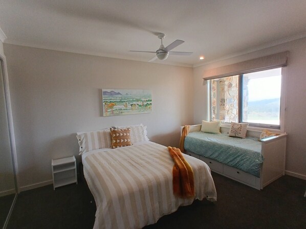 A bedroom with a bed, a window seat, a ceiling fan, and a painting on the wall.
