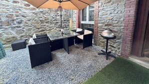 Une terrasse avec une table et des chaises, un grand parasol et une lampe.