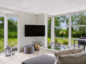 Ein modernes Wohnzimmer mit Flachbildfernseher, einem Glastisch und einer gemütlichen Sitzecke inklusive Sofa und Kissen.