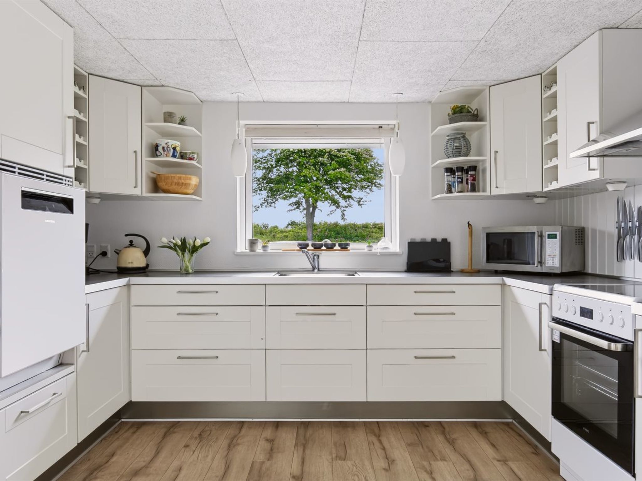 A modern kitchen with white cabinets, a large window, and a view of greenery outside.