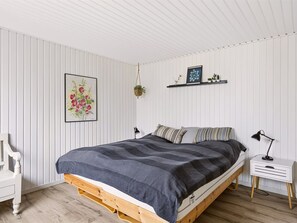 Un dormitorio con cama, mesitas de noche, una planta colgante y estante en la pared decorado con adornos.