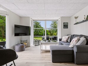 A modern living room with a grey sofa, a flat-screen TV, and a large window offering a view of greenery. - "Glum" - 300m from the sea by Interhome (Haderslev)