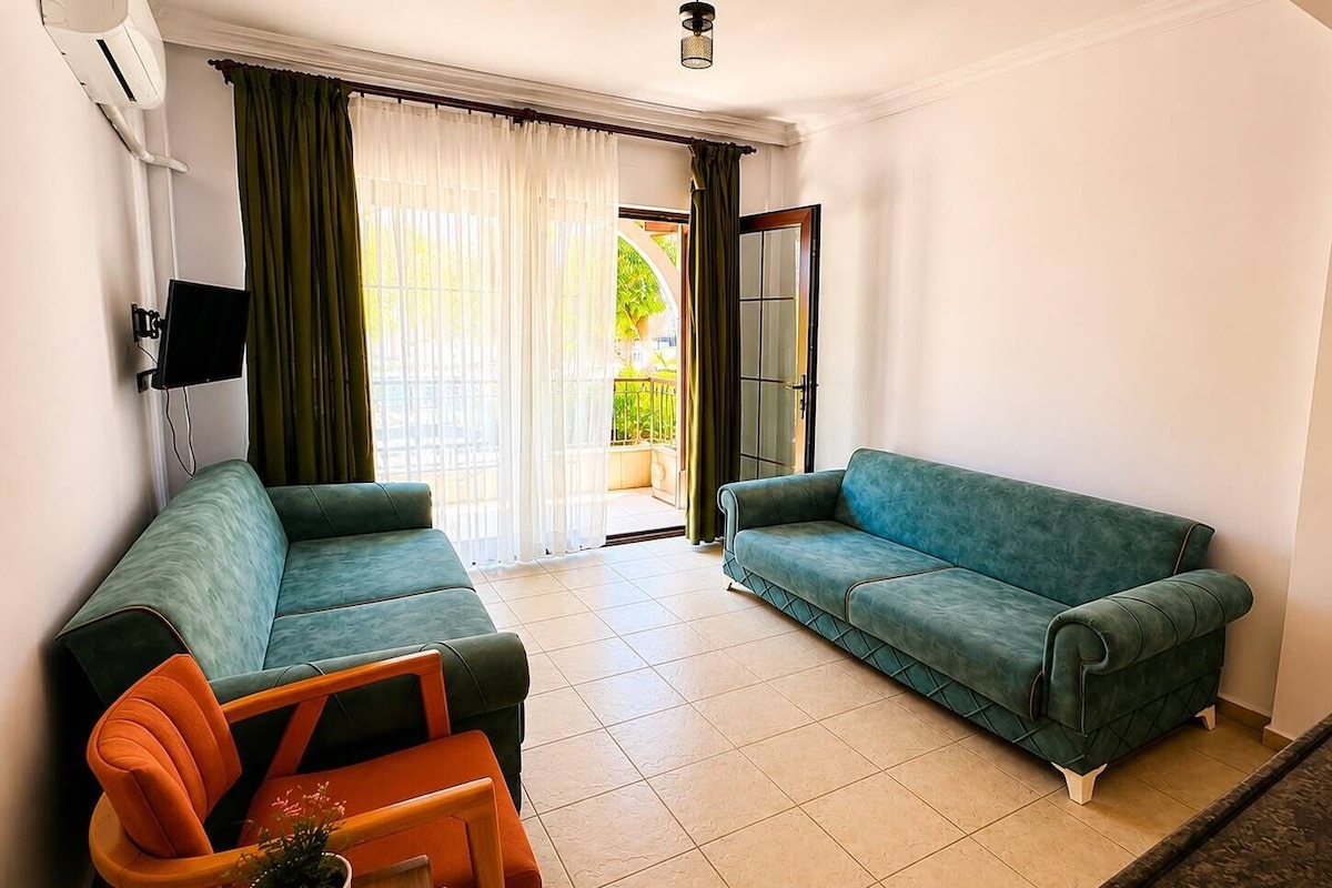 A living room with two sofas, a small table with a plant, and a sliding glass door leading to an outdoor balcony.
