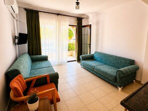 A living room with two sofas, a small table with a plant, and a sliding glass door leading to an outdoor balcony. - Lagoonia Sun Boutique Hotel (Ölüdeniz)
