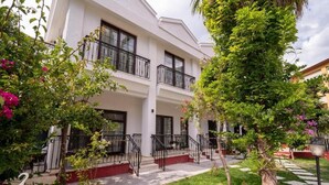 A two-story building with balconies, a garden with various plants, and a clear sky. - Lagoonia Sun Boutique Hotel (Ölüdeniz)