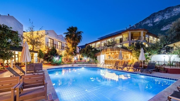 A swimming pool with lounge chairs and umbrellas, surrounded by buildings and a mountain backdrop. - Lagoonia Sun Boutique Hotel (Ölüdeniz)
