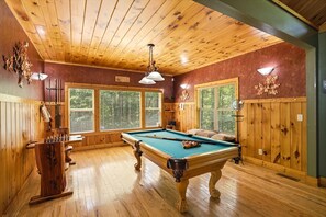 Ein Billardtisch in einem Raum mit Holzwänden und -decke, großen Fenstern und einer hölzernen Bank.