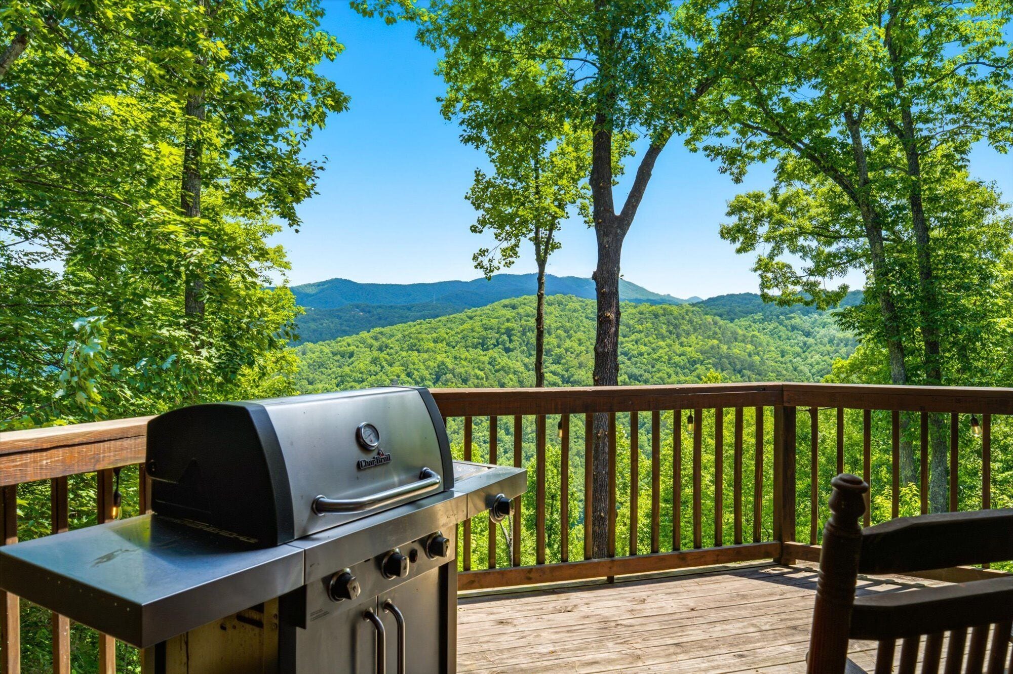 A barbecue grill on a wooden deck with a view of a forest and mountains.