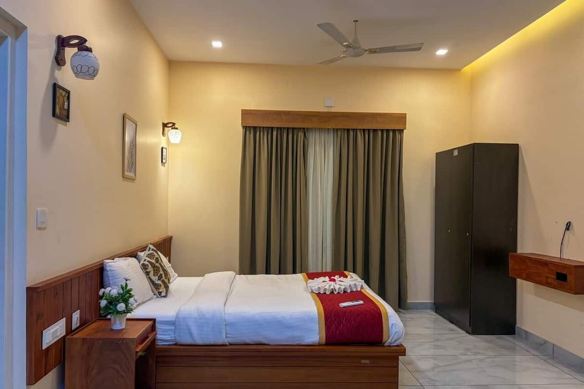 A hotel room with a bed, wooden headboard, bedside table, wall-mounted light, ceiling fan, and a dark-colored wardrobe.