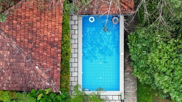 Une piscine sur le toit, avec un élément décoratif aquatique aux eaux bleues, entourée de verdure et surmontée d’un toit recouvert de tuiles rouges.
