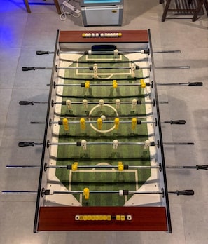 Uma mesa de futebol de botão com layout de campo de futebol, incluindo áreas de gol e figuras de jogadores.