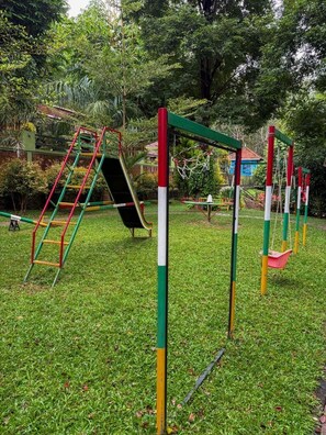 A playground with a slide, climbing structures, and swings. - Maple Grove Villa Resort (Panamaram)