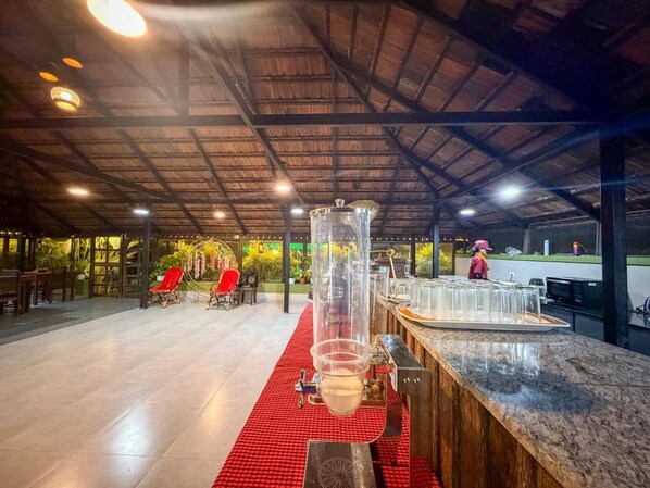 A bar area with a large cylindrical dispenser, red checkered tablecloth, and a counter with glasses.