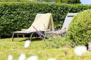 Dos sillones de descanso con una manta, rodeados de follaje y flores púrpuras.