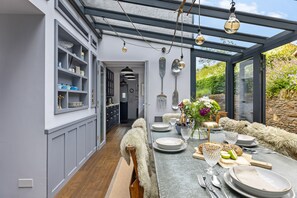 Eine moderne Küche mit Essbereich, mit einem langen Tisch für sechs Personen, einer eingebauten Schrankwand und Blick durch eine Glasverkleidung.