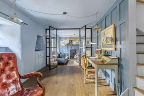 A room with a wooden floor, a red leather chair, a desk with a mirror, and a view into another room with a kitchen area. - East Cornworthy Cottage - Stylish Devon Retreat with Hot Tub, Fire Pit & Rolling Hill Views (East Cornworthy)