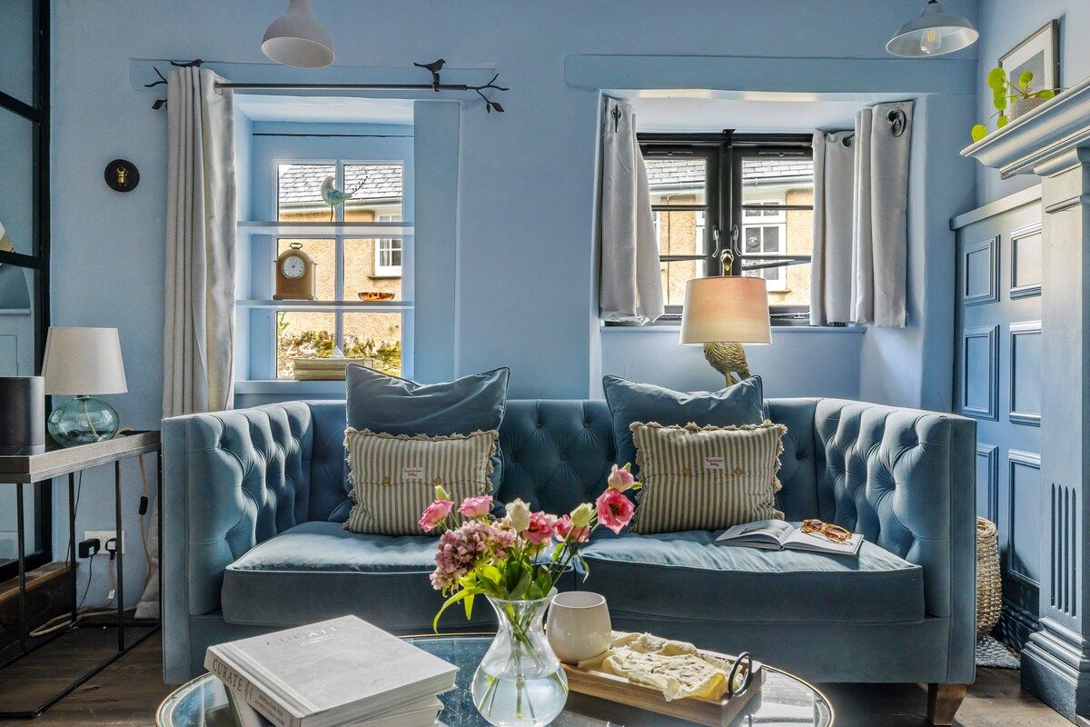 Un canapé bleu recouvert de tissu, agrémenté de coussins décoratifs, un vase rempli de fleurs et un livre posé sur une table d’appoint.