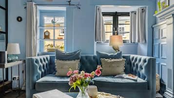 Un sofá tapizado en azul con almohadones decorativos, un florero con flores y un libro sobre una mesita.