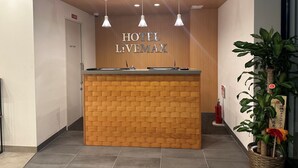 A hotel reception desk with a wooden design, overhead lighting, and a sign that reads 'HOTEL L'VEMAX'. - HOTEL LiVEMAX Namba WEST (Osaka)