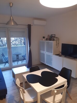 A modern living room with a dining area, a TV on a cabinet, and a balcony with chairs. - Cozy 1-bedroom apartment with AC in amazing Wrocław (Wrocław)