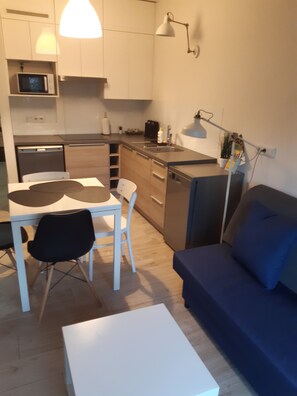 A compact living space with a kitchenette, a dining area with a table and chairs, a sofa, and a small white table. - Cozy 1-bedroom apartment with AC in amazing Wrocław (Wrocław)