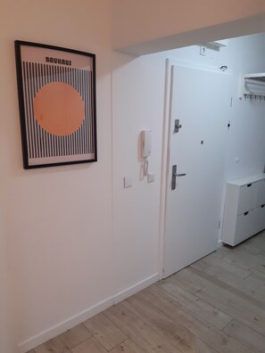 Ein Zimmer mit einem gerahmten Kunstwerk an der Wand, einer weißen Tür, einem Telefon und einem kleinen Schrank.