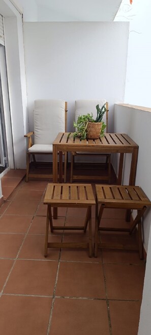 Ein Holztisch mit Stühlen auf einer gefliesten Terrasse, mit einem Blumentopf.