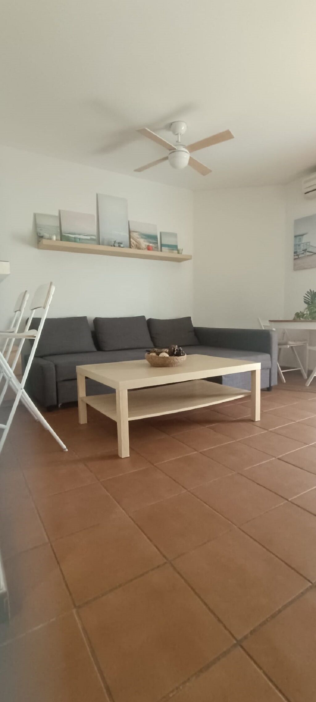 A living room with a sofa, a coffee table, a ceiling fan, and a wall-mounted shelf with artwork.